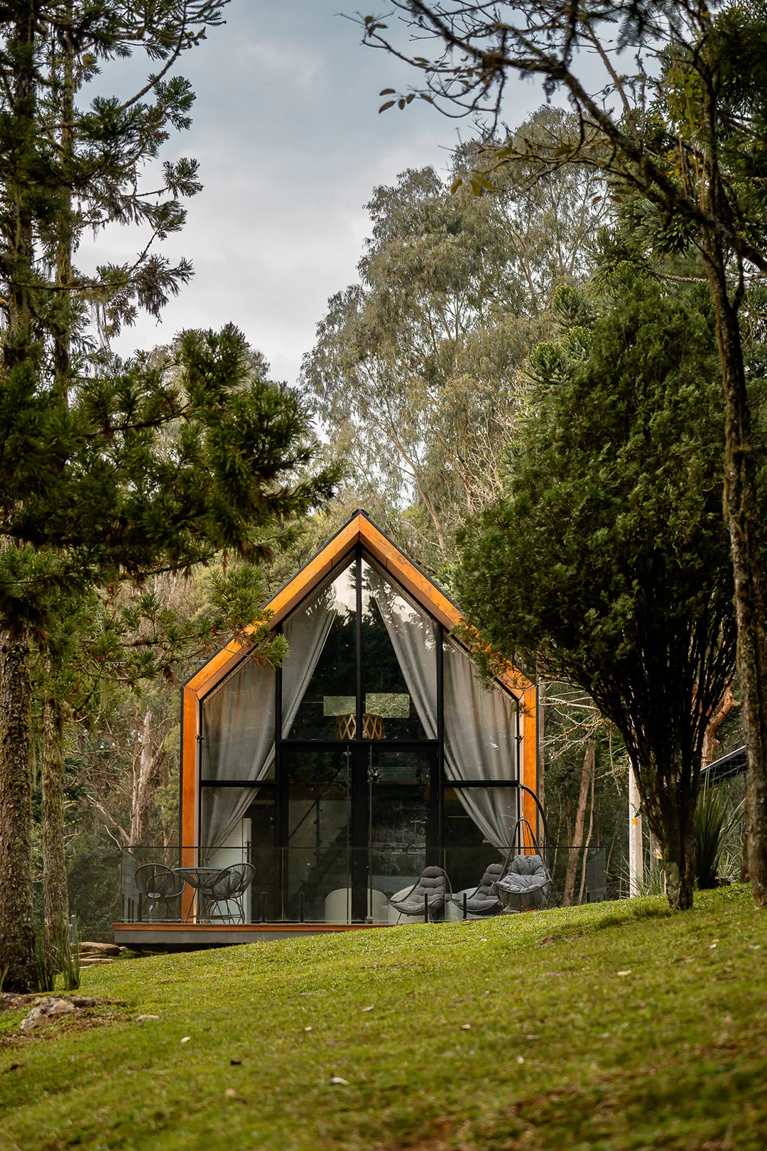 Lake house de fachada envidraçada no fim de um gramado, entre árvores altas