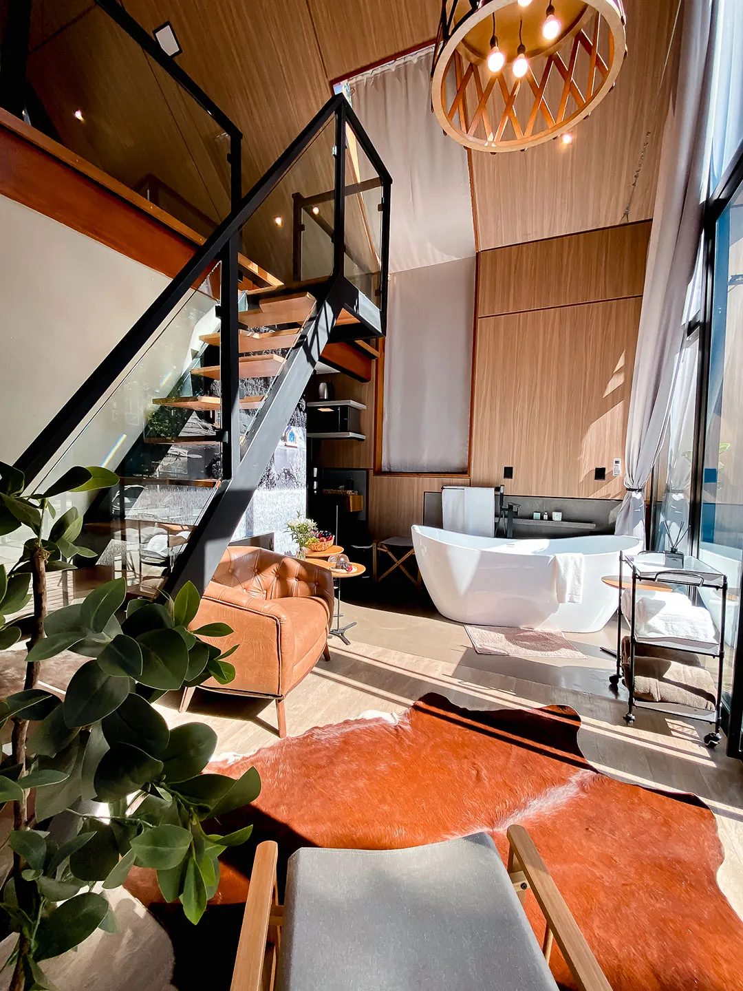 Interior visto da entrada: escada metálica, poltrona de couro, banheira e carrinho de toalhas, com planta em primeiro plano