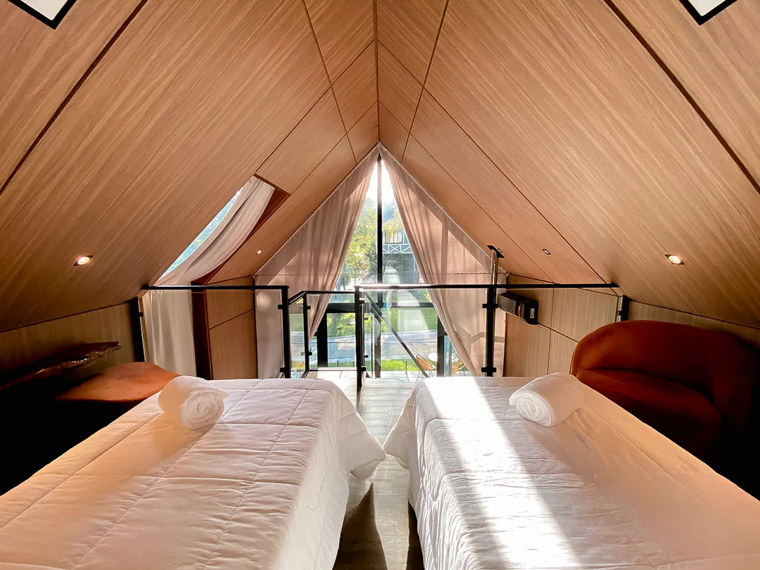 Duas camas de solteiro no mezanino voltadas para a janela triangular com cortinas abertas