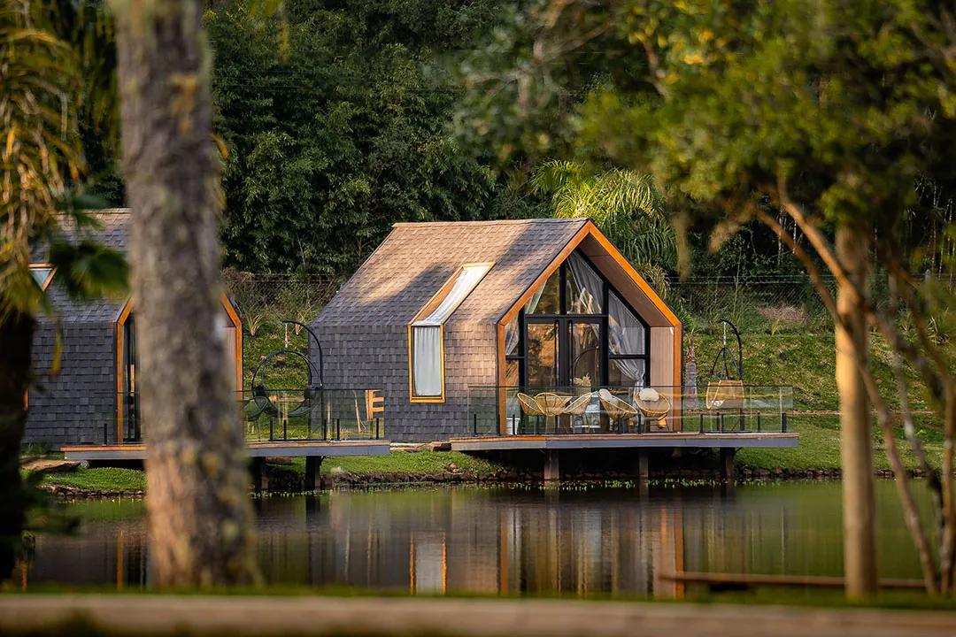 Lake houses com decks sobre o lago iluminadas pelo sol baixo, vistas entre troncos de árvores
