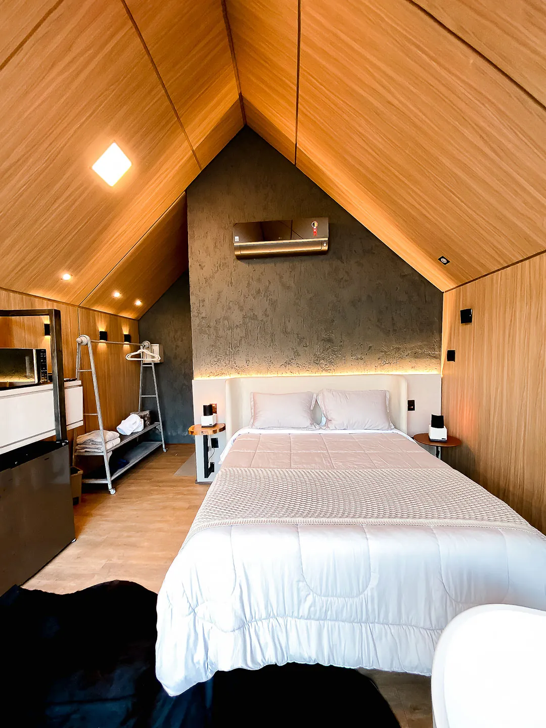 Cama queen de cabeceira estofada clara sob o telhado em A, com ar-condicionado e parede texturizada