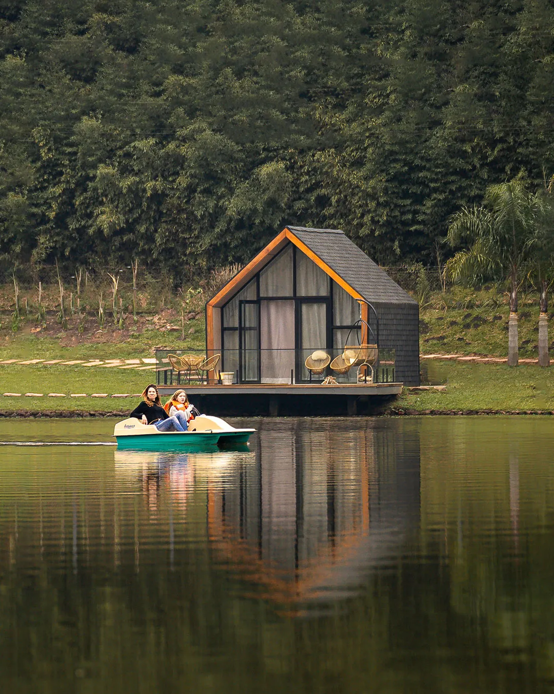 Lake house à beira do lago com deck e duas pessoas em um pedalinho à frente, refletidas na água